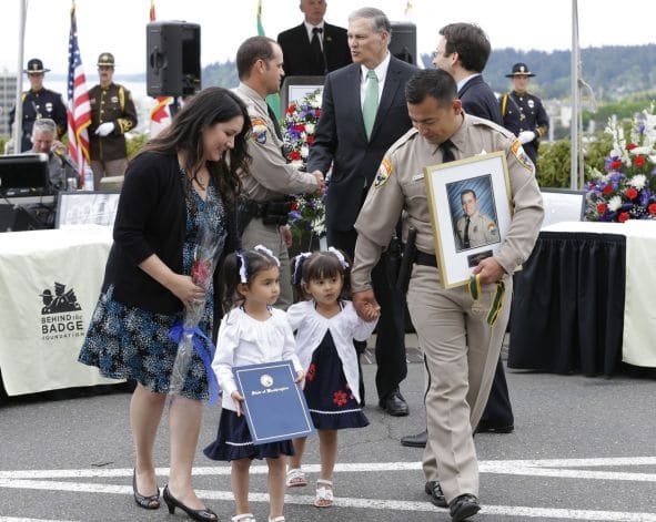 Adam Musgrove in uniform walking with his wife, Tina, and their two young daughters at a community memorial service.
